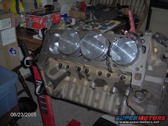 engine block with four pistons installed, sitting on an engine stand. Tools and parts are on a table in the background