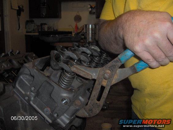 Engine valve train with a person using pliers on a valve spring