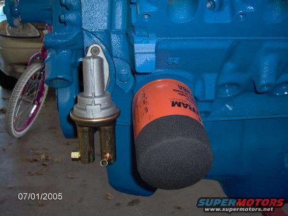 Blue painted engine block with silver fuel pump and orange FRAM oil filter. Bicycle wheel visible in background