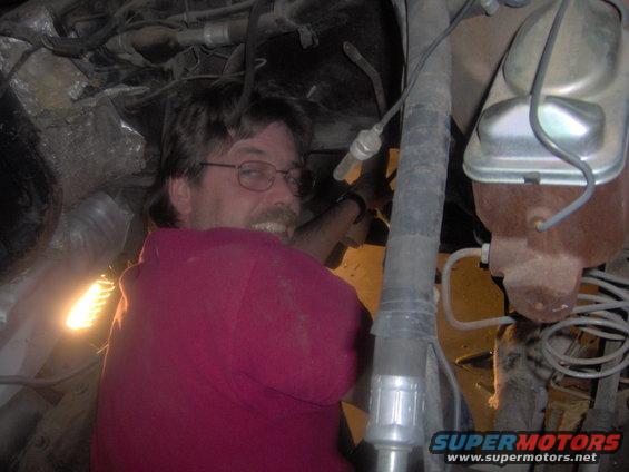 Man in red shirt working on vehicle engine bay, brake fluid reservoir visible