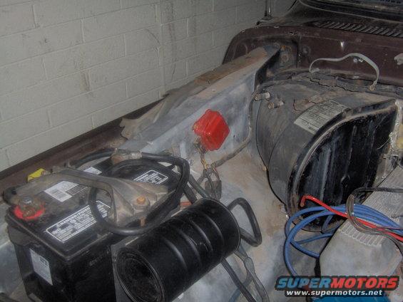 Car battery, air filter, and engine components in engine bay. Some wiring and a red distributor cap are visible