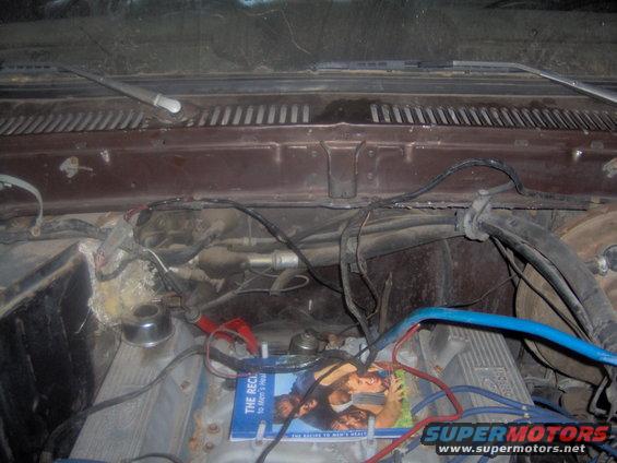 Engine bay with wires, hoses, and a magazine on the engine block