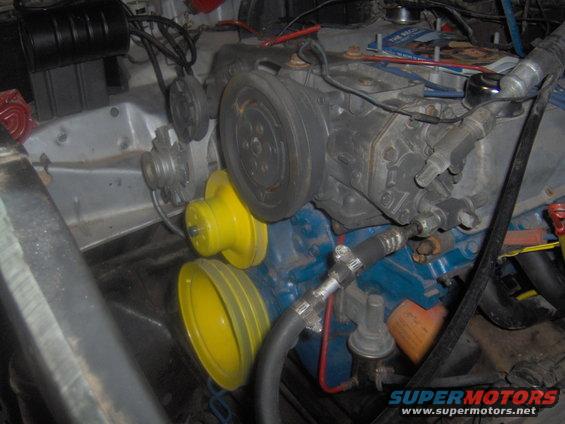 Engine compartment showing V-belts, pulleys, and engine block. Some parts are painted blue and yellow