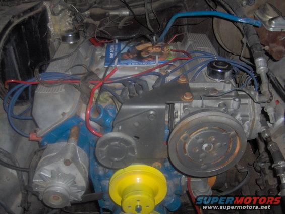 V8 engine bay with blue painted block, alternator, and pulley system. A magazine is on top of the engine