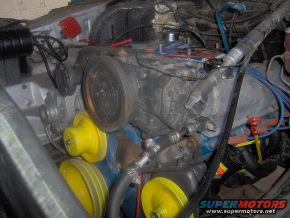 Engine bay showing V-belts, pulleys, and engine components. Yellow covers are visible on some pulleys