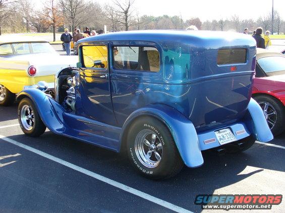 Blue hot rod sedan with large rear tires, parked next to a yellow and white car and a red sports car