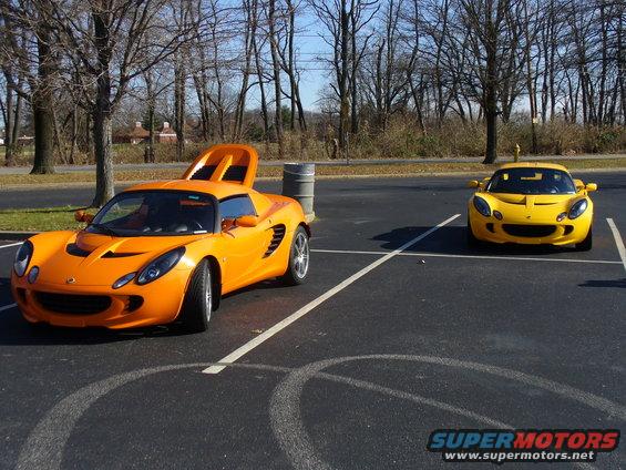 Orange sports car with rear engine cover open, parked next to a yellow sports car in a parking lot