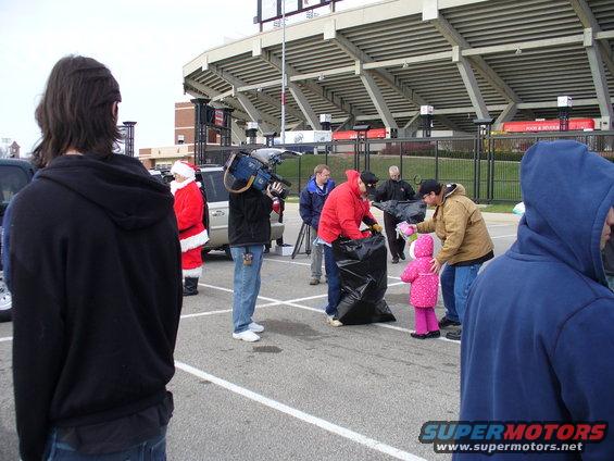 People in a parking lot with a stadium in the background, one person dressed as Santa