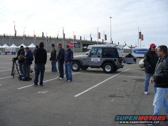 Group of people filming a gray Jeep Wrangler in a parking lot