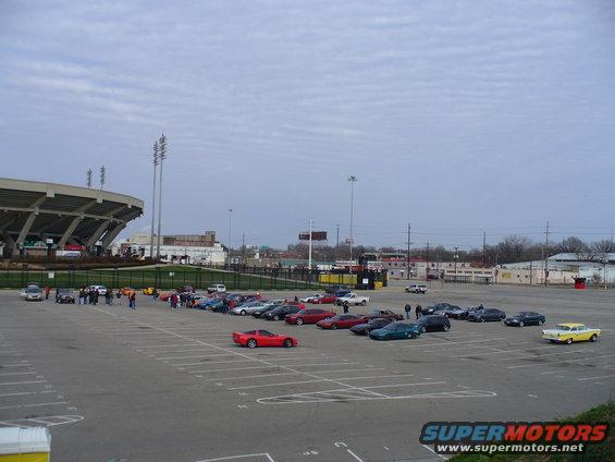 Parking lot with many cars, a stadium, and a yellow classic car