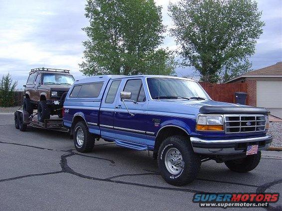 Blue 1995 Ford F-250 towing a lifted brown Ford Bronco II on a trailer