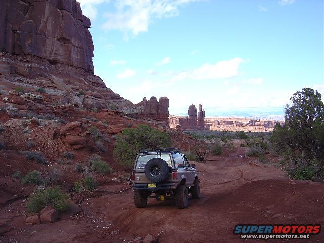 Brown Ford Bronco II with spare tire on rear, driving on dirt road in desert landscape