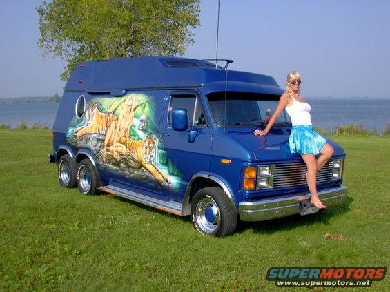 Blue custom van with tiger mural and dual rear wheels, woman posing on hood