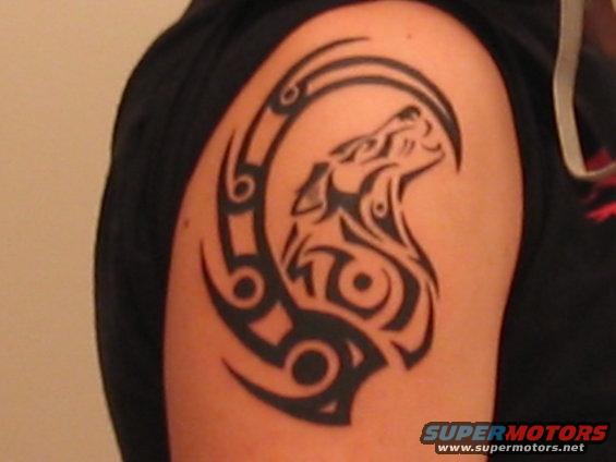 Tribal wolf tattoo on a person's arm. Supermotors.net logo in lower right