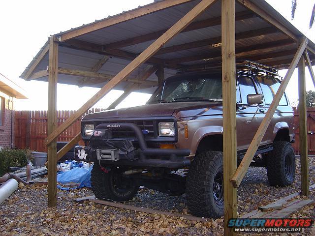 Brown Ford Bronco II with a winch on the front bumper, parked under a wooden carport