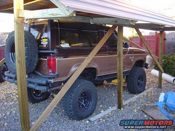 1986 Ford Bronco II parked under a wooden carport, spare tire mounted on rear door