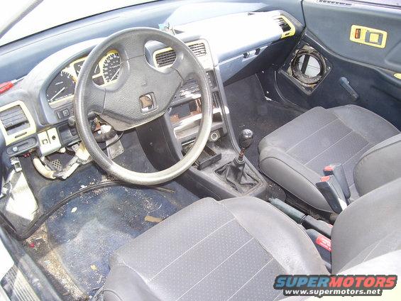 Interior view of a car with a manual transmission, showing the dashboard, steering wheel, and seats. The interior appears worn and dirty