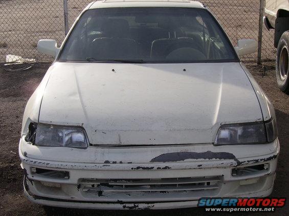 Front view of a white car with damaged front bumper and headlight. Appears to be a 1990s Honda CRX