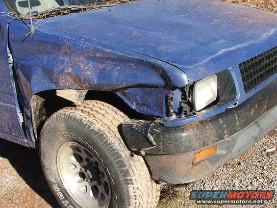 Front corner of a blue SUV showing significant damage to the fender, headlight area, and bumper