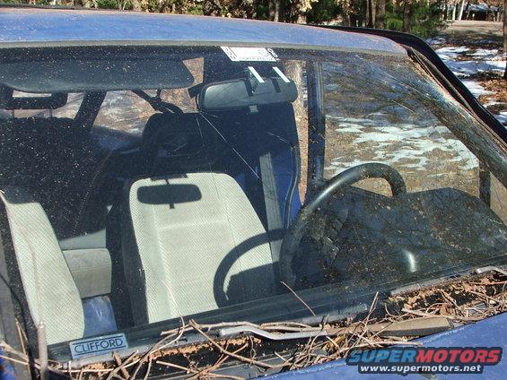 Blue car interior with cracked windshield, light-colored seats, and a steering wheel. A 'CLIFFORD' sticker is visible
