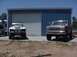 1988 Ford Bronco - Two SUVs are parked in front of a blue metal building. The SUV on the right appears to be a 1987 Ford Bronco.