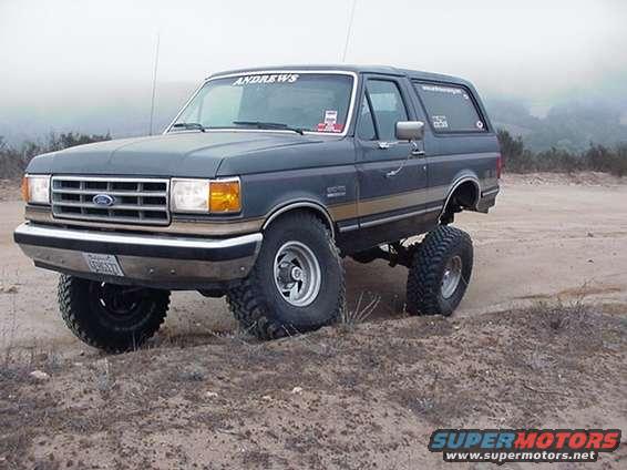 Dark blue Ford Bronco with lifted suspension and large tires on a dirt road
