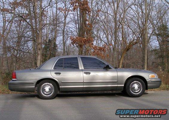 Side view of a silver 2001 Ford Crown Victoria parked on a road with trees in the background