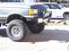 1988 Ford Bronco - A lifted pickup truck is parked on a paved surface, with a white SUV in the background.