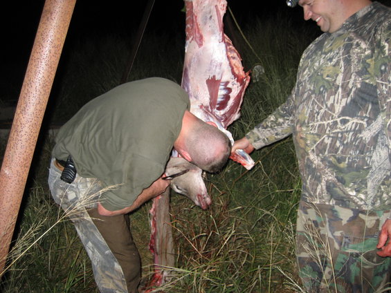 Two men butchering a deer carcass outdoors at night