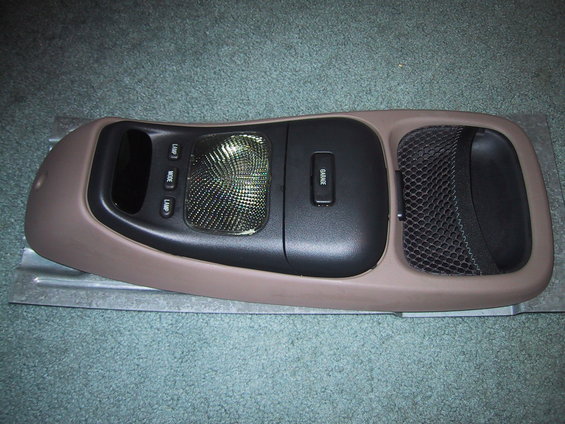 Overhead console assembly with lamp buttons, a textured light cover, and a garage door opener button