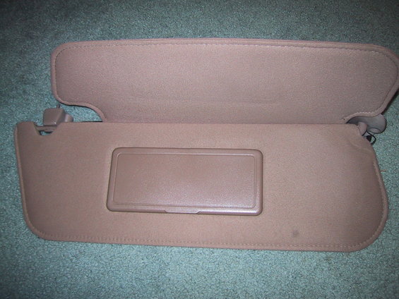 Tan sun visor with a rectangular vanity mirror cover, viewed from the front