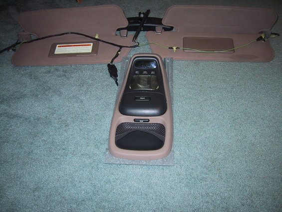 Overhead console and two sun visors with wiring, laid out on carpet