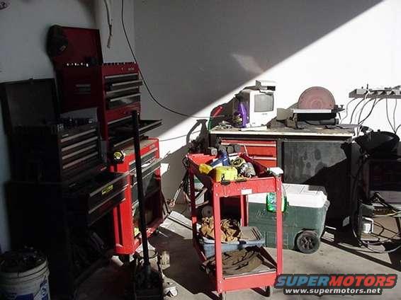 Garage interior with stacked toolboxes, a red rolling cart, a cooler, and a disc sander on a workbench