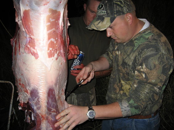Hanging deer carcass being processed by two men, one holding a can