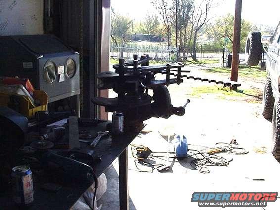 Workbench with tools, a vise, and a sandblaster cabinet. A large tire is visible outside