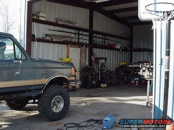 Gray Ford Bronco with tan stripe, lifted, large tires, parked in a garage