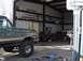 1988 Ford Bronco - A gray Ford Bronco with a tan stripe is parked inside a metal garage with various tools and equipment.