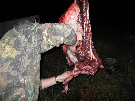 Person in camouflage butchering a large piece of meat outdoors at night