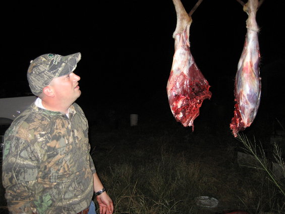 Man in camo looks at two deer legs hanging in the dark. One leg is torn open