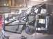 1988 Ford Bronco - A custom truck chassis with a roll cage and suspension components is shown in a workshop, with another vehicle in the background.