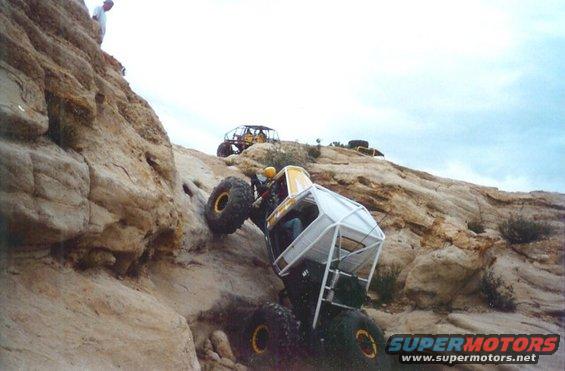 Yellow and white off-road buggy climbing steep rock face, another buggy behind