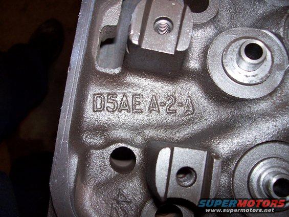 Close-up of a cast iron engine cylinder head with part number D5AE A-2-A stamped on it