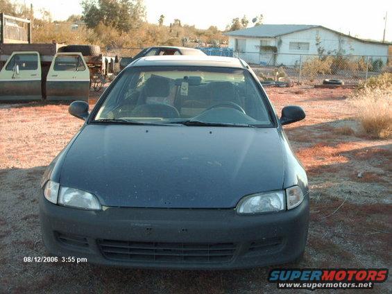 Dark blue sedan parked in a dry, outdoor lot with a white building in the background