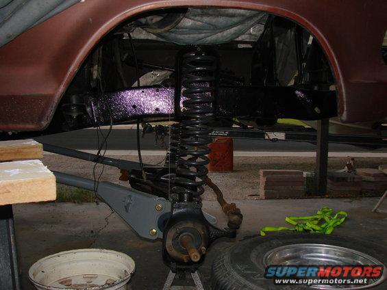 Red vehicle's front suspension and brake assembly on jack stands, showing a large coil spring and control arm