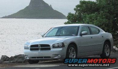 Silver Dodge Charger parked by the water with a mountain in the background