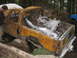 1990 Ford Bronco - A severely damaged pickup truck sits in a wooded area, with another vehicle partially visible.