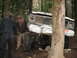 1990 Ford Bronco - An off-road vehicle appears to be stuck between trees, with two individuals assessing the situation.