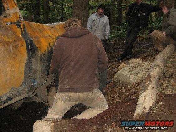 Yellow and black Ford Bronco stuck in mud, side view. People are gathered around
