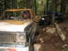 1990 Ford Bronco - Two off-road vehicles, one a heavily damaged pickup, are parked on a wooded trail.