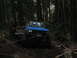 1990 Ford Bronco - Two vehicles are stuck in the mud in a dense forest, with one vehicle being pulled by a tow rope.